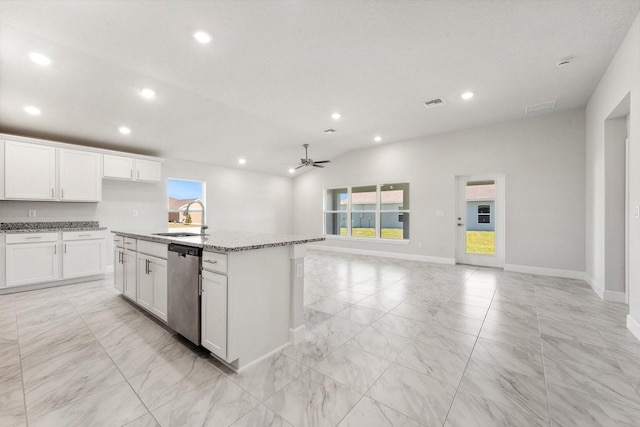 kitchen featuring ceiling fan, dishwasher, sink, light stone counters, and a center island with sink