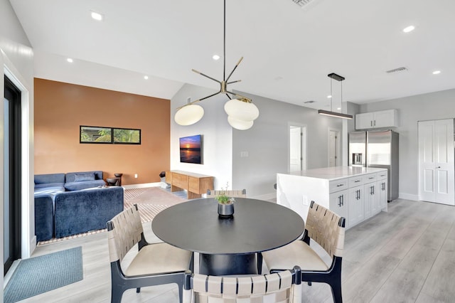 dining area with a chandelier, lofted ceiling, and light hardwood / wood-style flooring