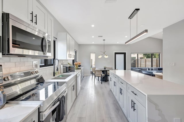 kitchen featuring light wood-type flooring, stainless steel appliances, sink, white cabinets, and hanging light fixtures