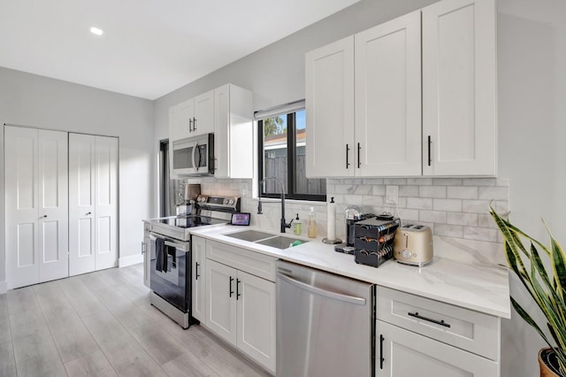 kitchen with sink, light hardwood / wood-style flooring, tasteful backsplash, white cabinetry, and stainless steel appliances