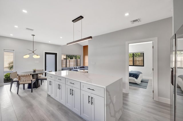 kitchen with light hardwood / wood-style flooring, white cabinets, a healthy amount of sunlight, and decorative light fixtures