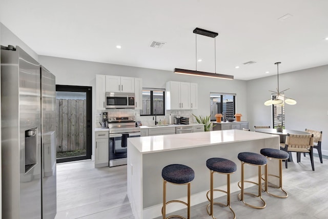 kitchen with white cabinets, appliances with stainless steel finishes, a kitchen island, and pendant lighting