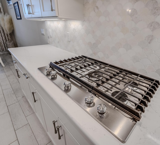 interior details featuring decorative backsplash, white cabinets, light stone counters, and stainless steel gas cooktop