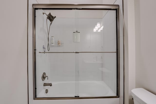 bathroom with toilet and shower / bath combination with glass door