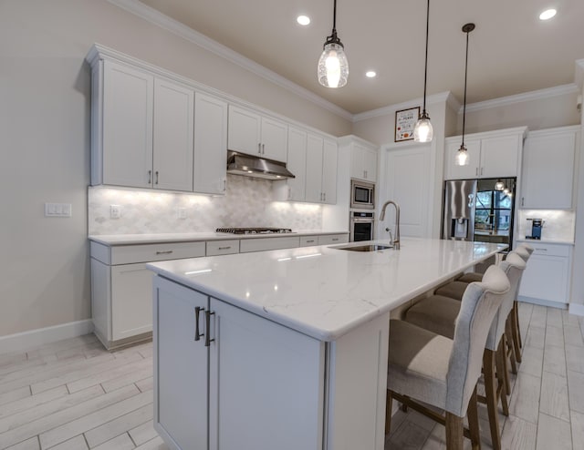 kitchen with appliances with stainless steel finishes, tasteful backsplash, a kitchen island with sink, white cabinets, and hanging light fixtures