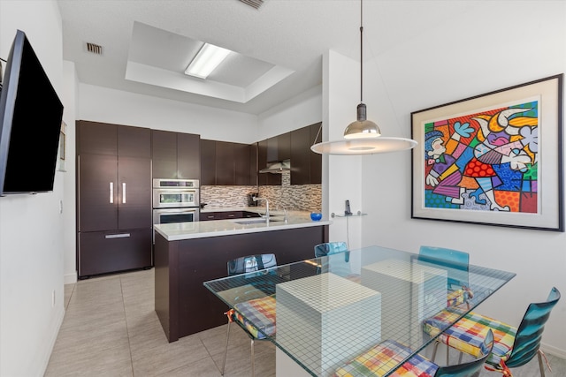 kitchen with decorative backsplash, dark brown cabinetry, extractor fan, sink, and hanging light fixtures