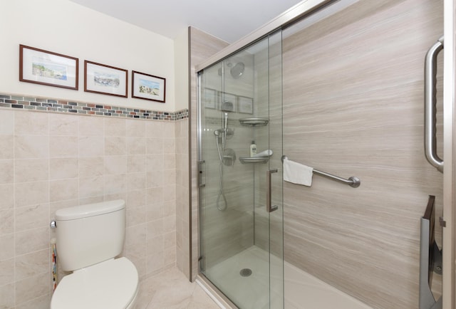 bathroom with toilet, tile walls, and a shower with shower door