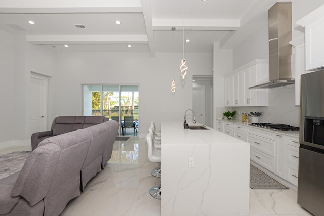 kitchen with wall chimney range hood, sink, appliances with stainless steel finishes, hanging light fixtures, and white cabinets