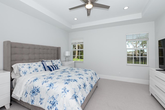 bedroom with ceiling fan, light colored carpet, and a raised ceiling