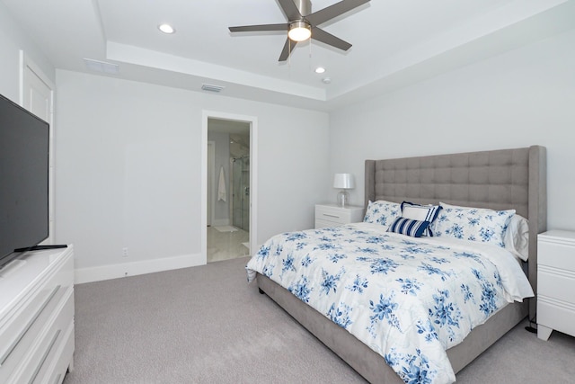 bedroom featuring ceiling fan, light colored carpet, connected bathroom, and a tray ceiling