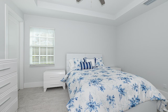 bedroom featuring visible vents, baseboards, a tray ceiling, light carpet, and a ceiling fan