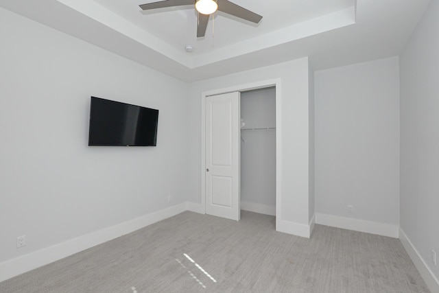 unfurnished bedroom featuring a closet, light colored carpet, a raised ceiling, and ceiling fan