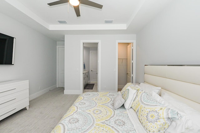 bedroom with light carpet, a tray ceiling, a walk in closet, and ceiling fan