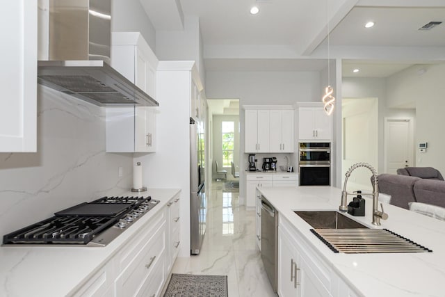 kitchen featuring pendant lighting, wall chimney range hood, white cabinetry, stainless steel appliances, and light stone countertops