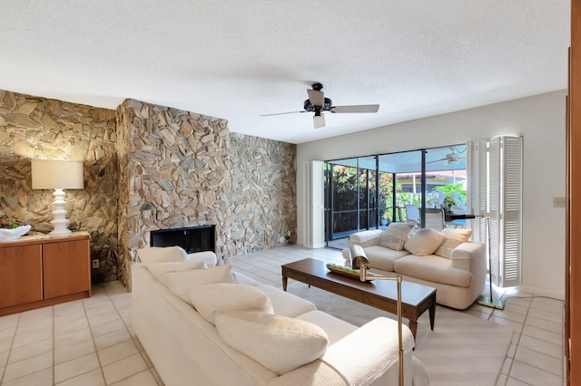 living room with a textured ceiling, a stone fireplace, ceiling fan, and light tile patterned flooring