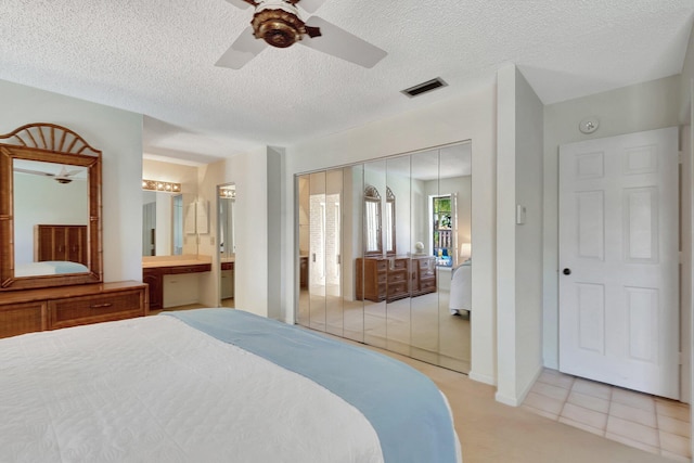 bedroom featuring ceiling fan, a closet, light tile patterned flooring, and ensuite bath