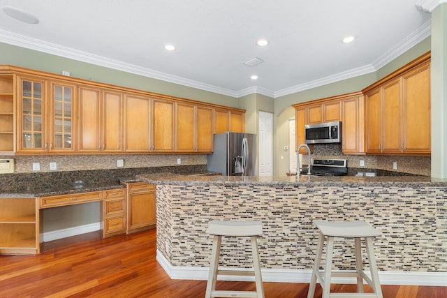 kitchen with kitchen peninsula, appliances with stainless steel finishes, crown molding, and dark stone counters