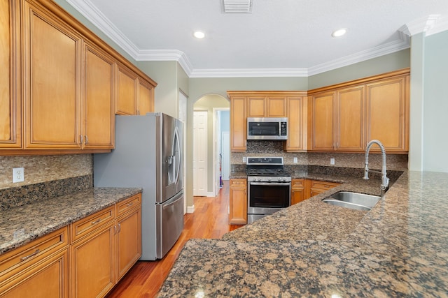 kitchen featuring dark stone counters, sink, stainless steel appliances, and ornamental molding