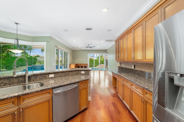 kitchen with dark stone counters, sink, ceiling fan, ornamental molding, and stainless steel appliances