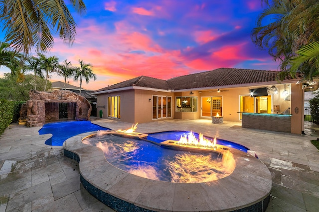 pool at dusk featuring an in ground hot tub, pool water feature, ceiling fan, and a patio area