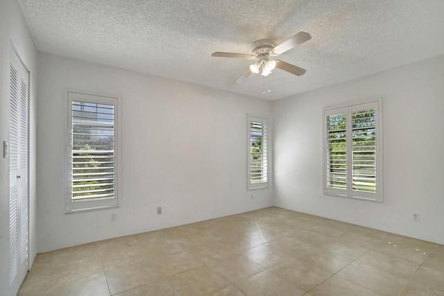 empty room with ceiling fan, light tile patterned floors, and a textured ceiling