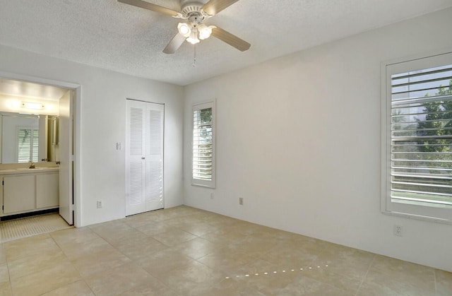 unfurnished bedroom with ensuite bathroom, a textured ceiling, ceiling fan, sink, and a closet