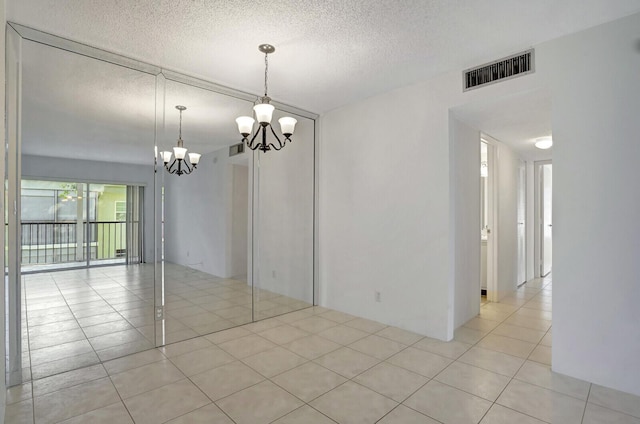 tiled empty room featuring a textured ceiling and a notable chandelier