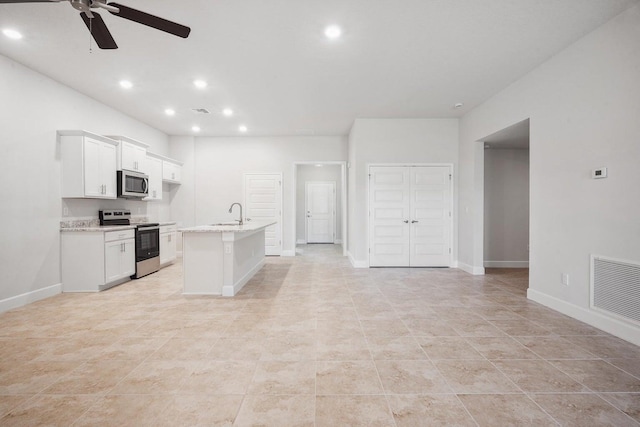 kitchen with a center island with sink, ceiling fan, appliances with stainless steel finishes, light stone counters, and white cabinetry