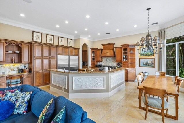 791 NE Marine Dr, Boca Raton, FL 33431 - kitchen with built in refrigerator, open shelves, premium range hood, brown cabinetry, and tasteful backsplash