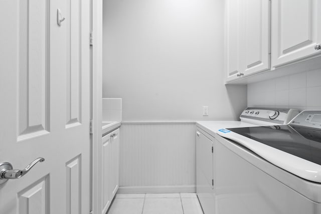 clothes washing area with cabinets, light tile patterned floors, and washer and dryer