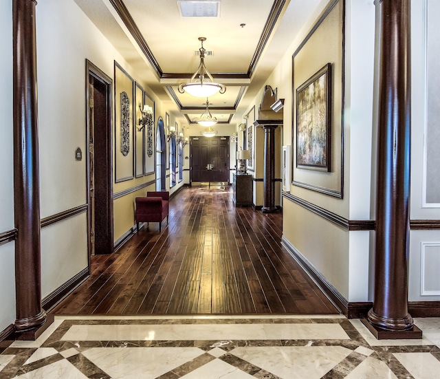 hallway with a tray ceiling, ornate columns, dark hardwood / wood-style floors, and ornamental molding