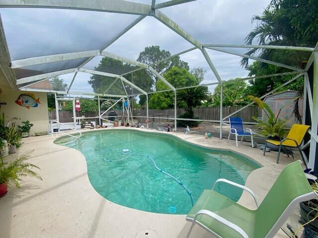 view of pool featuring glass enclosure, a storage shed, and a patio area