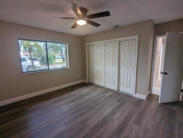 unfurnished bedroom with a textured ceiling, dark hardwood / wood-style flooring, a closet, and ceiling fan