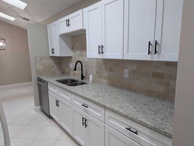 kitchen with light stone countertops, a skylight, stainless steel dishwasher, sink, and white cabinets