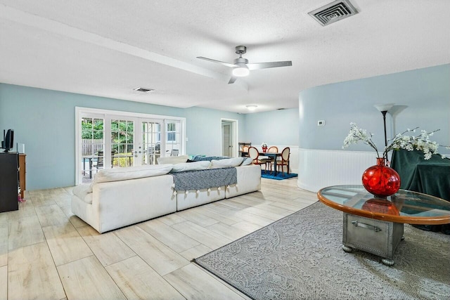 living room with ceiling fan, french doors, a textured ceiling, and light wood-type flooring