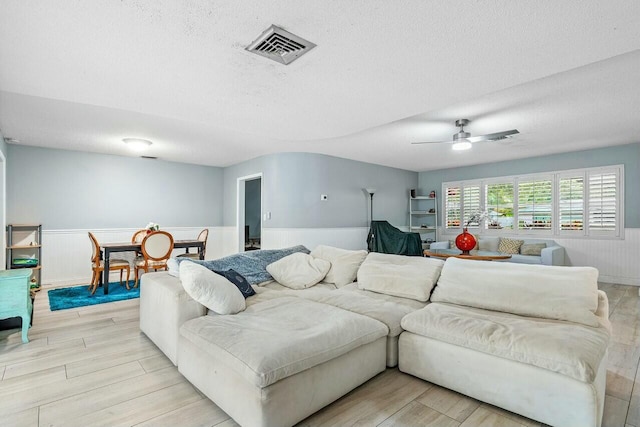 living room with ceiling fan, a textured ceiling, and light wood-type flooring