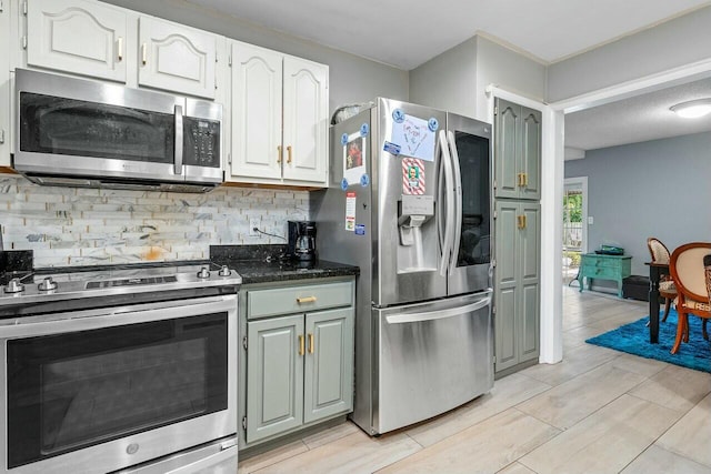 kitchen featuring light hardwood / wood-style flooring, dark stone counters, decorative backsplash, white cabinets, and appliances with stainless steel finishes