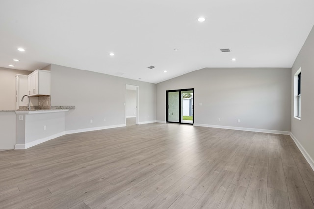 unfurnished living room featuring baseboards, a sink, vaulted ceiling, and light wood finished floors