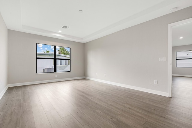 empty room featuring recessed lighting, a raised ceiling, baseboards, and wood finished floors