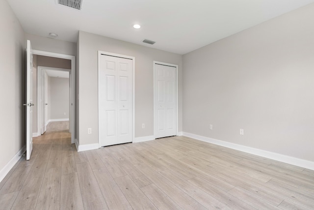 unfurnished bedroom featuring baseboards, two closets, visible vents, and light wood-style floors