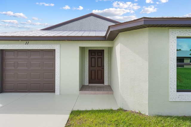 property entrance with metal roof, a garage, concrete driveway, stucco siding, and a standing seam roof