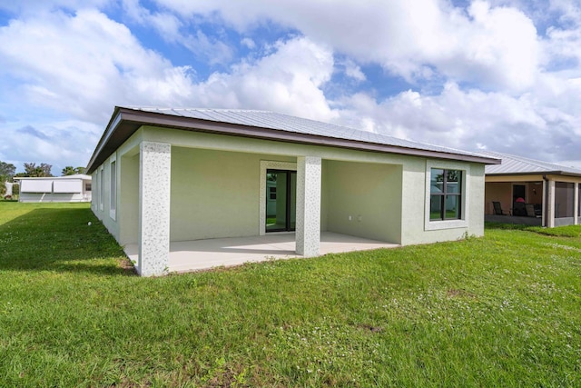 rear view of house with stucco siding, a lawn, and a patio