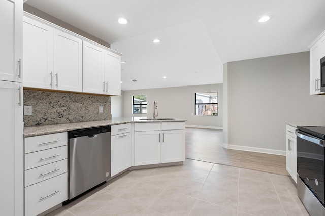 kitchen featuring stainless steel appliances, a peninsula, a sink, white cabinets, and decorative backsplash