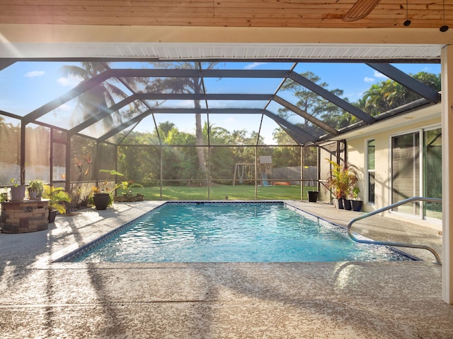 view of pool featuring a yard, a playground, glass enclosure, and a patio area