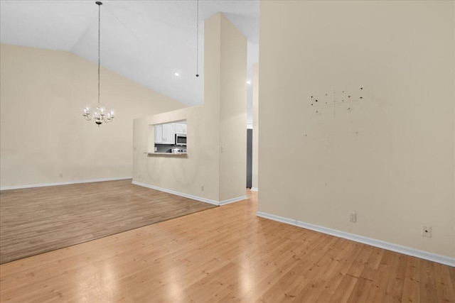 unfurnished living room with high vaulted ceiling, light wood-type flooring, and an inviting chandelier