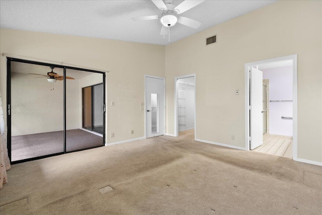 unfurnished bedroom with a closet, light carpet, ceiling fan, ensuite bathroom, and lofted ceiling