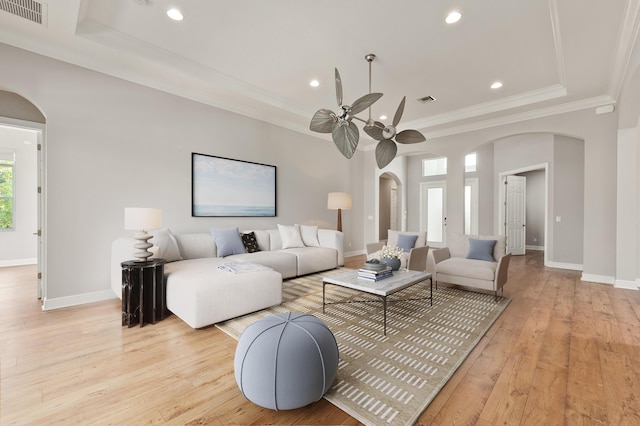 living room with ceiling fan, a raised ceiling, crown molding, and light hardwood / wood-style flooring