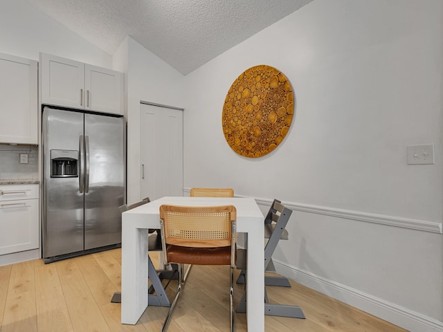 dining area with vaulted ceiling, light hardwood / wood-style floors, and a textured ceiling