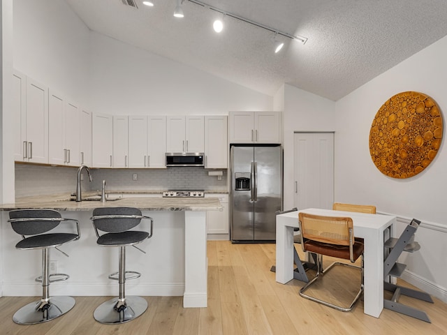 kitchen featuring stainless steel appliances, a kitchen breakfast bar, light stone counters, backsplash, and white cabinets