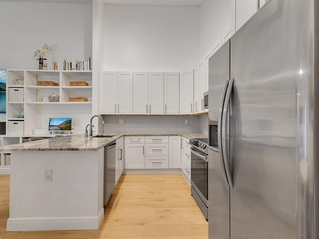 kitchen featuring stainless steel appliances, kitchen peninsula, stone countertops, white cabinets, and light wood-type flooring